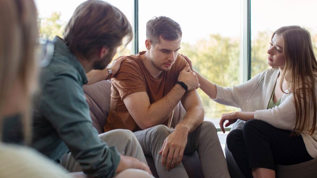 Young man wondering "Can you overdose on antidepressants?" during a group meeting with friends.